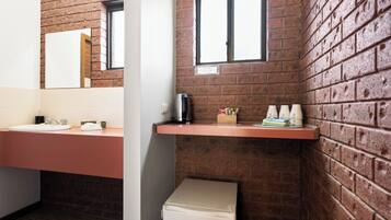 A bathroom with a brick wall, a sink, a mirror, a window, and a small refrigerator.