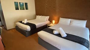 Habitación de hotel con dos camas, un muro decorativo de ladrillo y una lámpara en el techo.