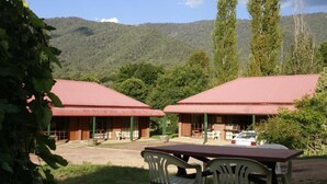 Dos edificios con techo rojo y terraza al aire libre, rodeados de vegetación y con una montaña al fondo.