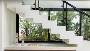 Una escalera moderna con barandillas de vidrio y vistas a plantas tropicales.