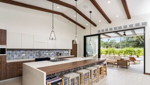 Una cocina moderna con una isla grande, taburetes de bar y vistas a una zona de piscina.