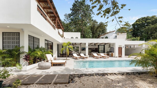 Una casa moderna con piscina, sillas de descanso y un patio rodeado de plantas.