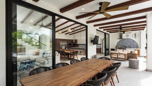 Un comedor amplio con una larga mesa de madera y sillas de mimbre negro, una cocina con electrodomésticos modernos y un gran ventanal con vistas al exterior.