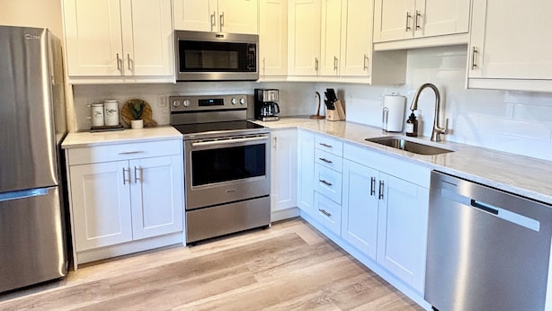 A modern kitchen with white cabinets, stainless steel appliances, and a wooden floor.