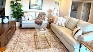 A living room with a sofa, a coffee table, a side table, a lamp, a plant, and a television.