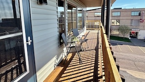 A covered porch with a wooden floor, a metal railing, and a view of a building in the background.