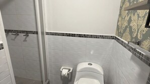 Une salle de bain comprenant des toilettes, une douche et un espace de douche fermé par des parois en verre.
