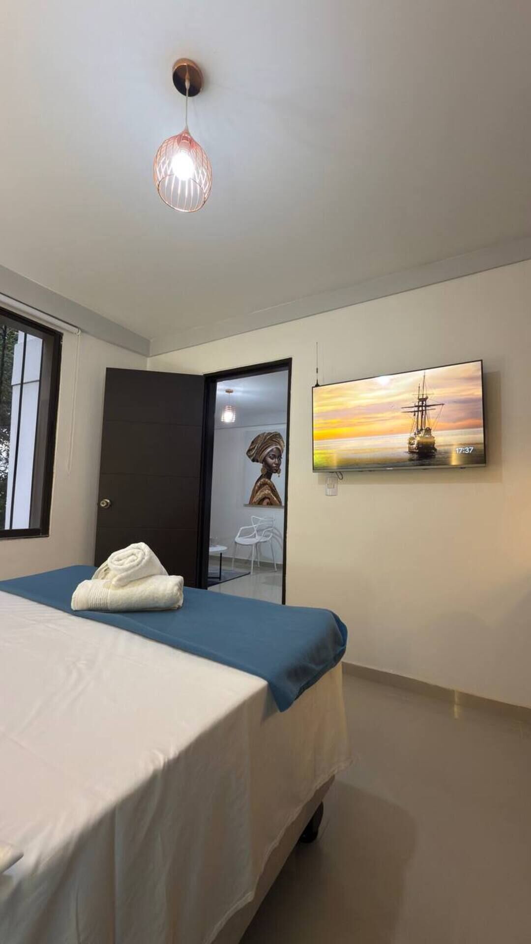 A bedroom with a bed, a painting, a TV, and a door.