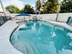 A swimming pool with a stone waterfall feature, a blue umbrella, and a chair. - Spacious 3-bedroom house with pool in a peaceful area in Bakersfield. (Bakersfield)