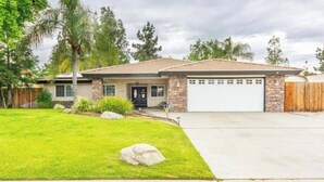 A single-story house with a garage, a front lawn with a rock, and a wooden fence. - Spacious 3-bedroom house with pool in a peaceful area in Bakersfield. (Bakersfield)