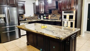 A modern kitchen with dark wood cabinets, stainless steel appliances, and a granite island. - Spacious 3-bedroom house with pool in a peaceful area in Bakersfield. (Bakersfield)