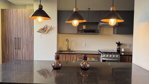 A modern kitchen with dark wood cabinets, a granite countertop, and pendant lighting. - Alba by Pardela (Guadalajara)