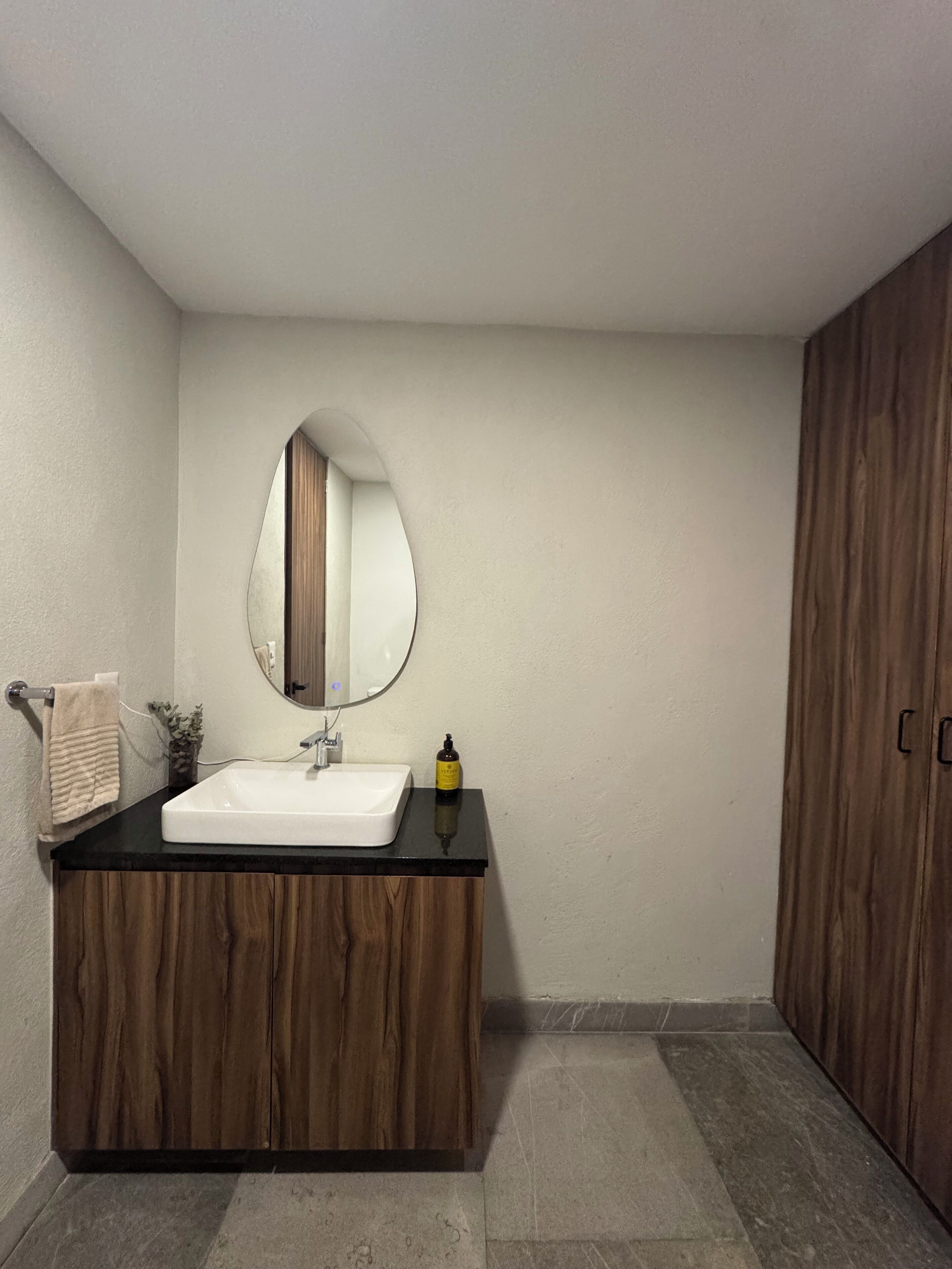 A bathroom with a white sink, wooden vanity, a round mirror, and a towel rack.