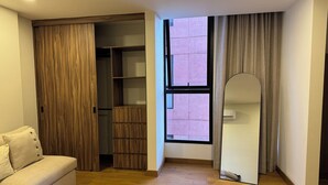 A room with a wooden floor, a white sofa, a wooden wardrobe, a window with curtains, and a mirror. - Alba by Pardela (Guadalajara)