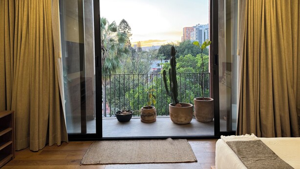 A room with a large sliding glass door leading to a balcony with potted plants and a view of the cityscape. - Alba by Pardela (Guadalajara)