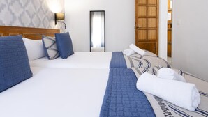 Ein Hotelzimmer mit zwei Betten, einem Nachttisch, einer Wandlampe, einem Spiegel und einer Holztür.