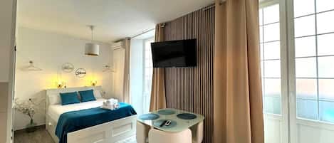 Een moderne hotelkamer met een bed, een televisie, een tafeltje en een raam met gordijnen.