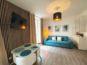 Un salon moderne avec un canapé bleu, une table en verre, un téléviseur à écran plat fixé sur un panneau en bois et un luminaire suspendu.