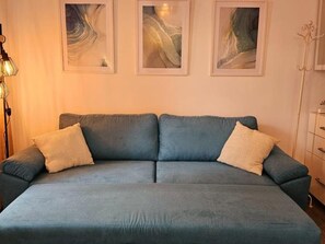 A room with a blue sofa, two pillows, and three abstract paintings on the wall.