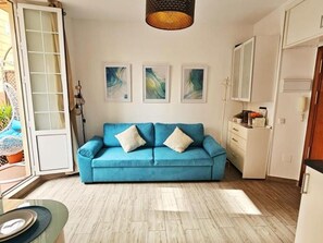 Un saló amb un sofà blau, una zona de menjador amb una taula de vidre i una cuina amb armaris blancs.