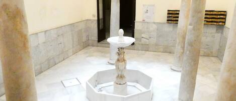 Ein Atrium mit Marmorboden, einer zentralen Fontäne, Säulen und einem Rundbogenportal.