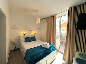 A bedroom with a bed, bedside lamps, a hanging light fixture, a window with curtains, and a wall-mounted TV. - Sol de M Laga (Málaga)