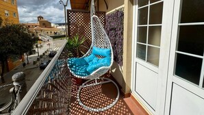 A balcony with a white hanging chair, a lattice fence, and a view of buildings.