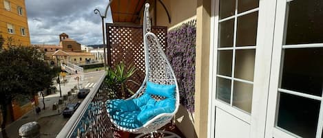 Un balcon avec un fauteuil suspendu blanc, une clôture en treillis et une vue sur les immeubles.