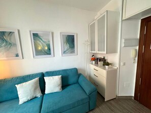 Een kamer met een smaragdgroene bank, een witte kast en drie abstracte schilderijen aan de muur.
