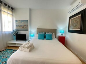 Una habitación de hotel con una cama, un televisor, un cuadro y una mesita de noche roja.