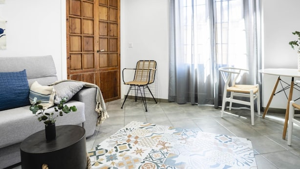 A living room with a grey sofa, a black coffee table, a patterned rug, a wooden door, and a window with grey curtains. - 7 Condes 4 (Málaga)