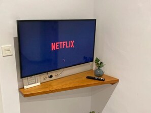 A television on a wooden shelf with a remote control and a small plant beside it. - 7 Condes 4 (Málaga)