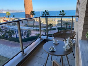 A balcony with a table set for tea, overlooking a beach with palm trees and a clear view of the sea.