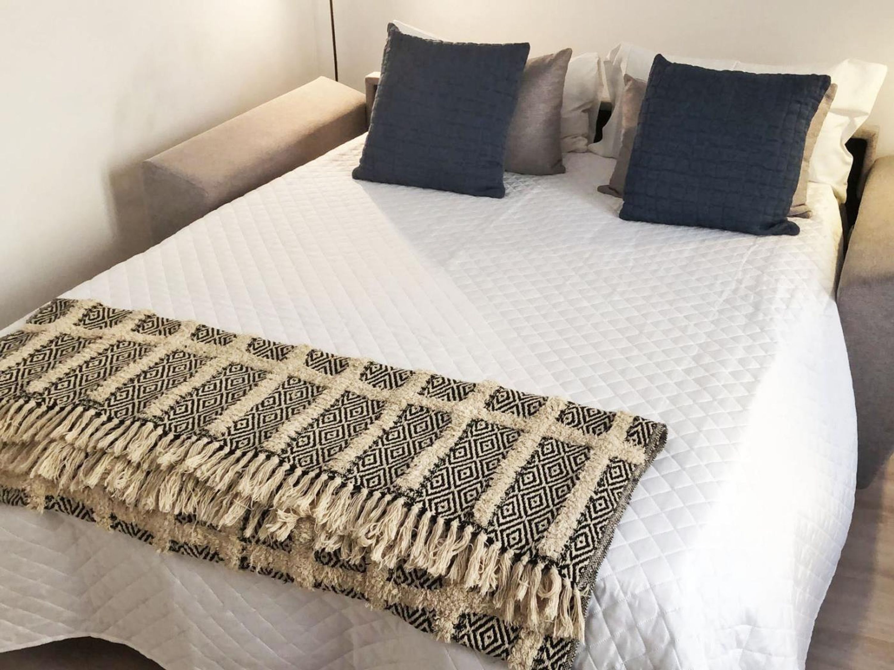 Una cama bien hecha con una manta estampada, una mesita de noche y almohadas a juego.