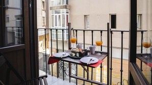 Ein Balkon mit Tisch, gedeckt für zwei Personen, mit einem Teller Essen, einem Glas Orangensaft und einem Glas Weißwein.