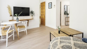 Ein modernes Wohnzimmer mit einem Holzesstisch, weißen Stühlen, einem an der Wand montierten Fernseher und einem gemusterten Teppich.