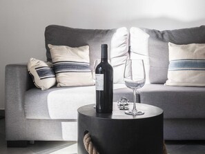 A modern living room with a grey sofa, striped pillows, a round black side table, a wine bottle, and an empty wine glass. - 7 Condes 5 (Málaga)