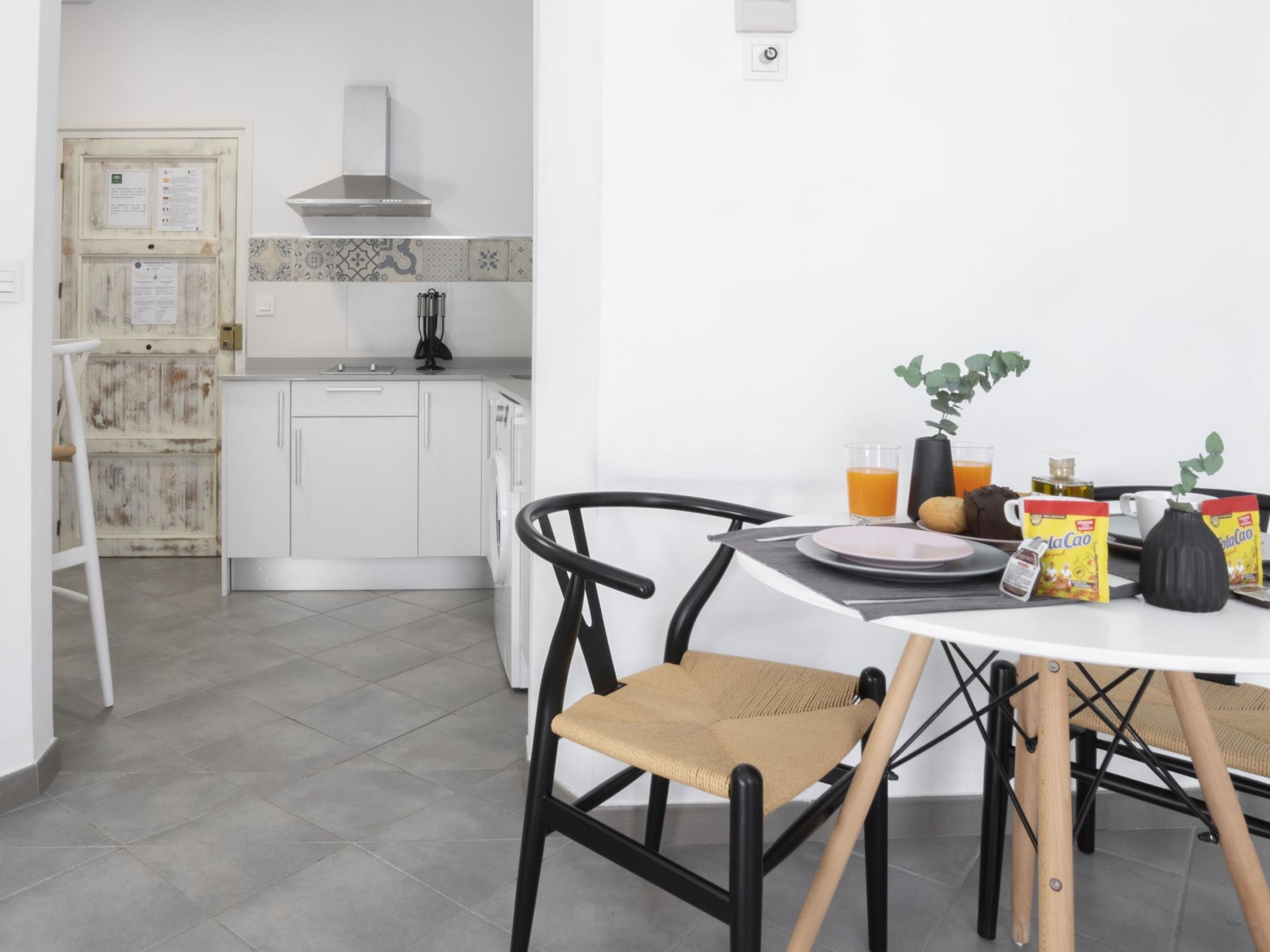 A modern kitchen with white cabinets, a stainless steel range hood, and a dining area with a table set for breakfast.