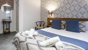 Een hotelkamer met een bed, nachtkastje, lamp, spiegel en een badkamer met wastafel en handdoekrek.