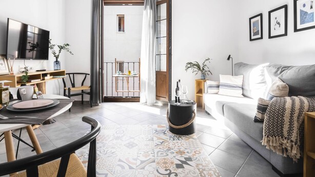 Een moderne woonkamer met een eethoek, een aan de muur bevestigde televisie en een bank met een plaids.
