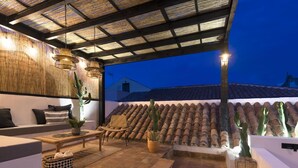 Un patio al aire libre con zona de estar, techo de fibras vegetales y cactus en macetas.
