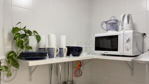 A kitchen with white tiles, a microwave, a kettle, and various utensils. - Santelmo 16 (Málaga)