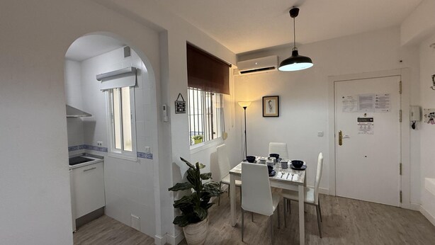 A compact kitchen with a stove, a dining area with a table set for four, and a potted plant. - Santelmo 16 (Málaga)