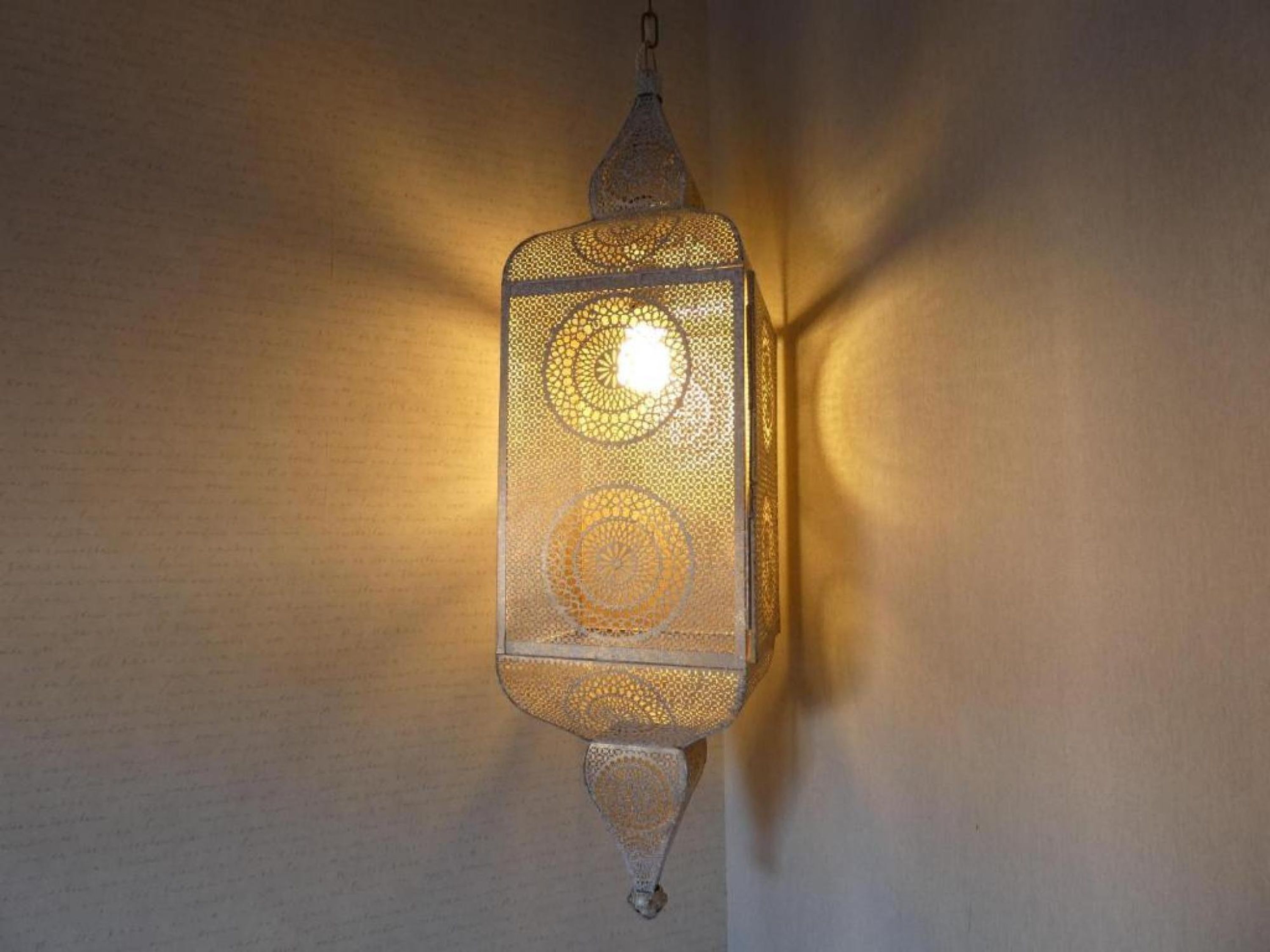 Un farol de pared con diseños elaborados y una cadena colgante.