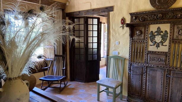 A rustic interior with a wooden bench, a chair, a decorative cabinet, and a vase with feathers. - Casa Rural del Jardin (Priego de Córdoba)