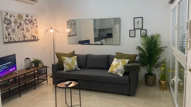 A modern living room with a grey sofa, a small round table, a floor lamp, and a TV. - Apartamento en el Centro Hist Rico (Málaga)