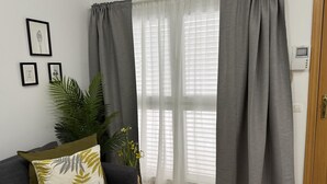 A living room with a grey sofa, a large plant, and a window with grey curtains. - Apartamento en el Centro Hist Rico (Málaga)