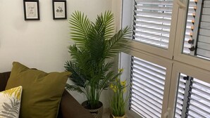A living room with a brown sofa, green and yellow pillows, a potted plant, and a window with blinds. - Apartamento en el Centro Hist Rico (Málaga)