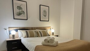 A neatly made bed with a brown blanket and rolled towels, two bedside lamps, a wooden headboard, and two framed botanical prints on the wall. - Apartamento en el Centro Hist Rico (Málaga)