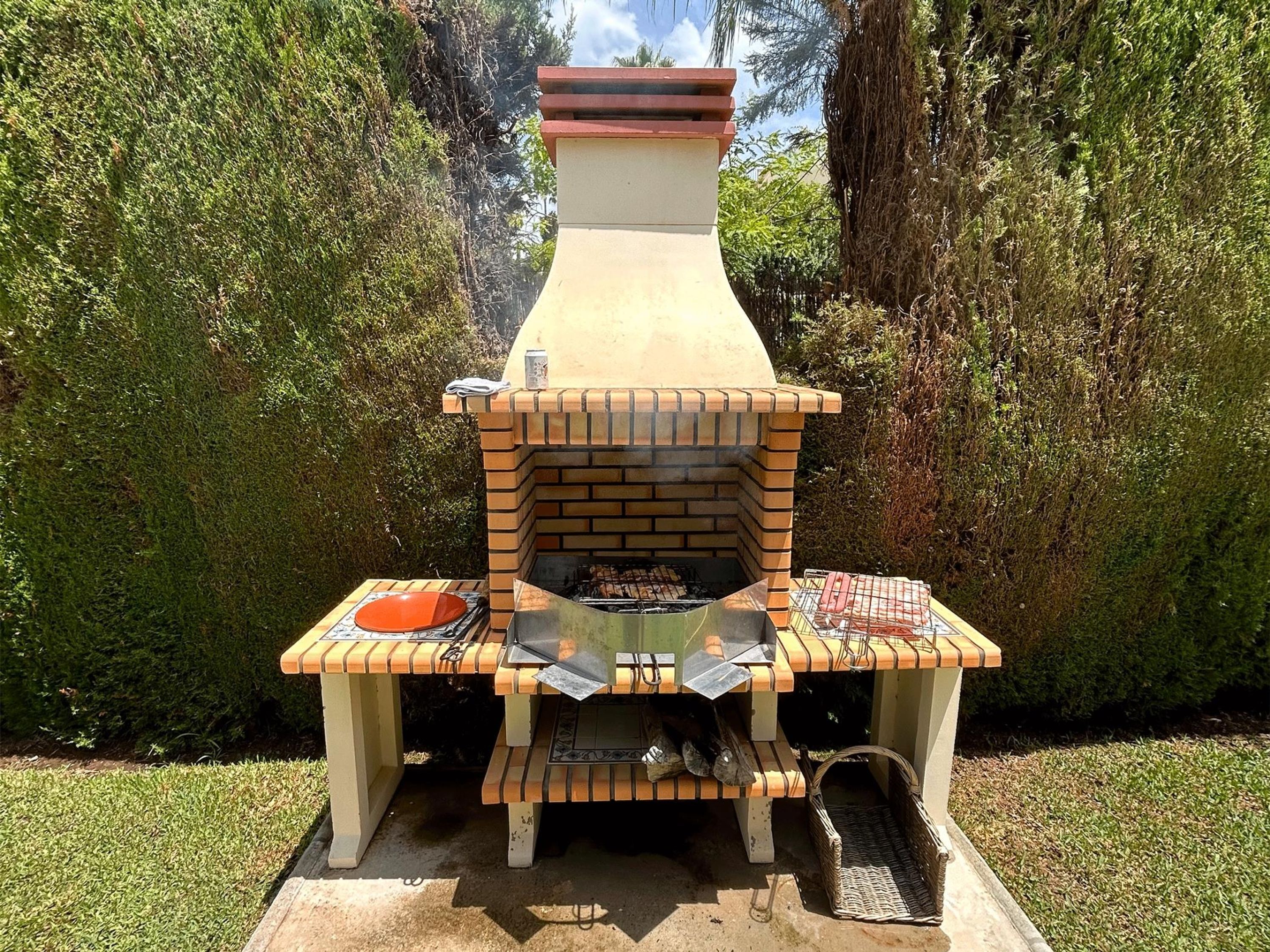 Una parrilla de ladrillo con chimenea, una mesa con una cesta y una bandeja para asar.